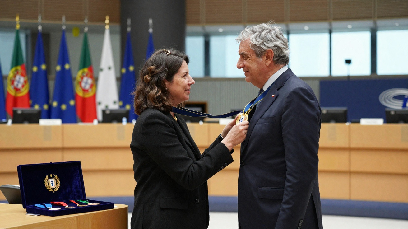 Mulher entrega medalha a homem em cerimónia formal com bandeiras de Portugal ao fundo.